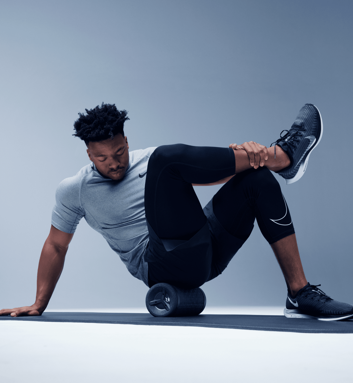 Man seated on a mat rolling his lower leg over a vibration roller